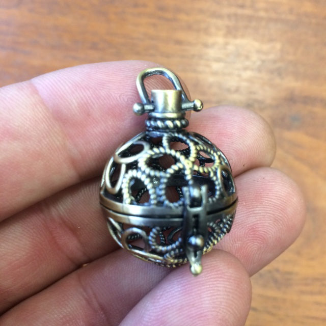 Pendentif/ Cage à pierre, peut servir de Bolas (pendentif de grossesse) ou pour perle de lave pour huile essentielle ! 2,5 centimètres de diamètre. Fait en laiton ! Vendu avec une perle de lave de 10mm !