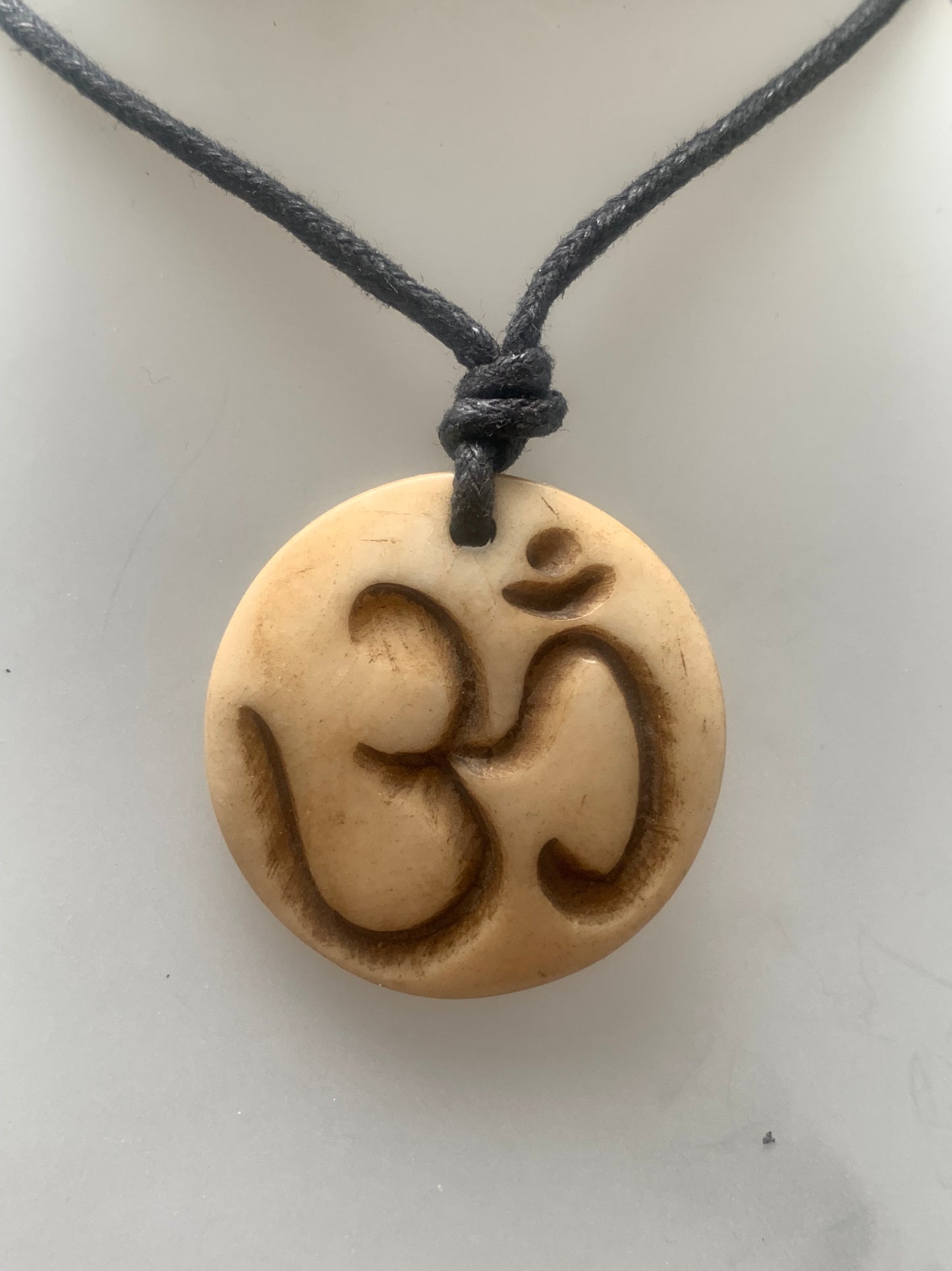 Pendentif artisanal du Népal avec symbole Om, sculpté dans de l’os, de 30 millimètres de diamètre x 4 mm d'épaisseur. Vendu avec cordon noir réglable offert, parfait !