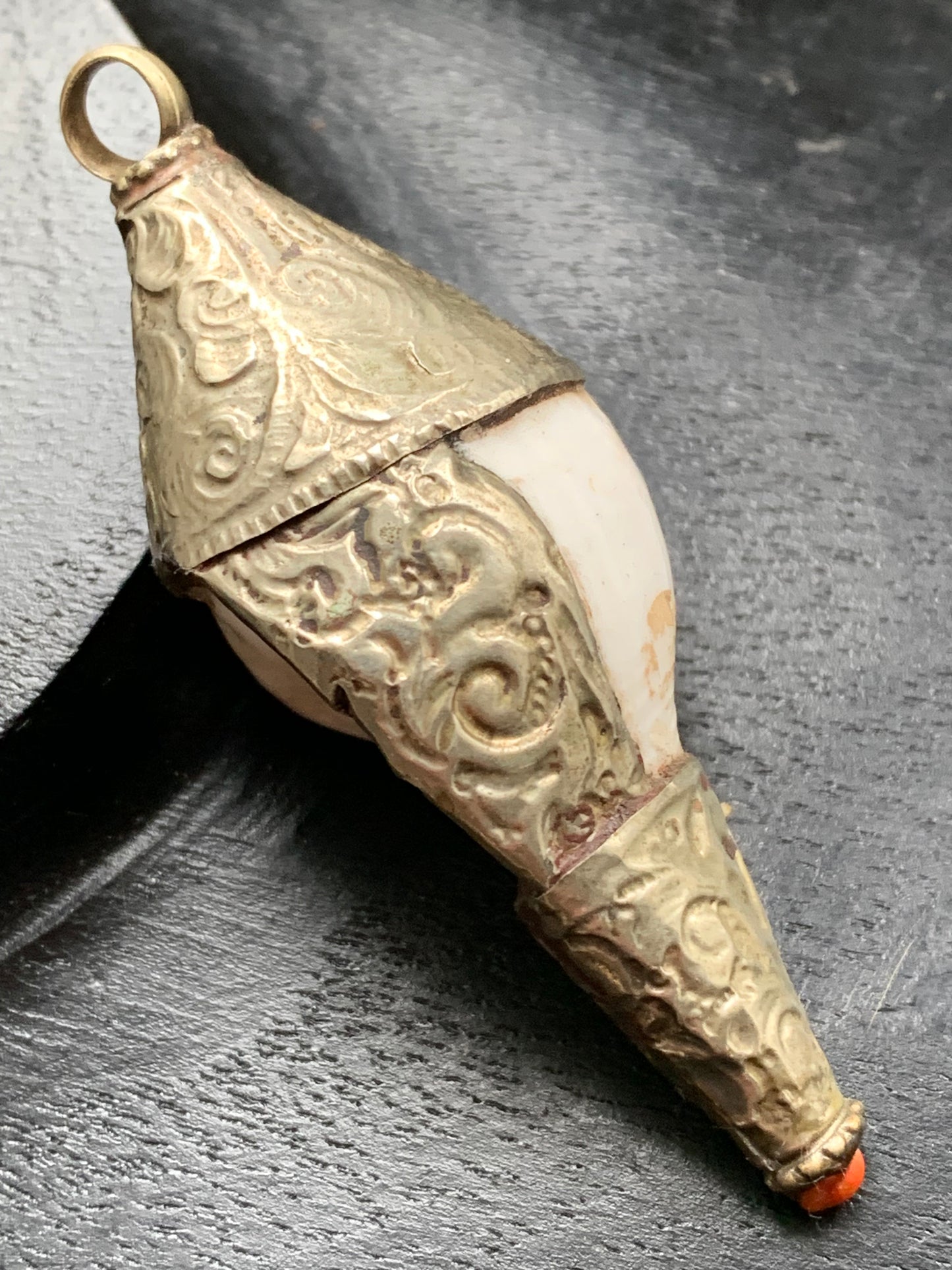 Pendentif artisanal du Népal en coquillage sertis en métal avec de jolies gravures et une perle de corail ! De 65 millimètres de hauteur x 28 mm de diamètre. Vendu avec cordon noir réglable offert, parfait !
