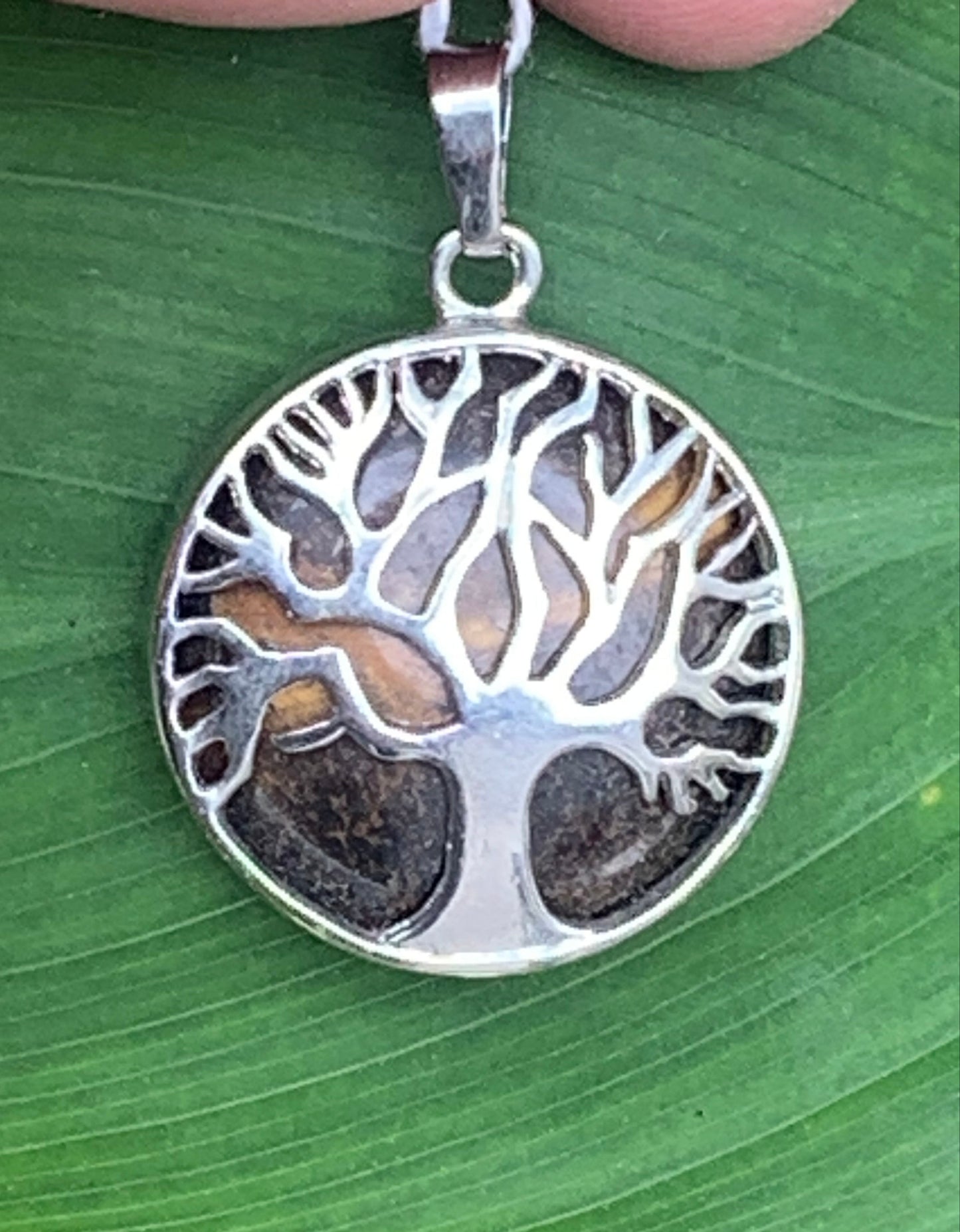 Pendentif en métal argenté 'Arbre de vie' avec un oeil de tigre en fond, de 27 mm de diamètre. Vendu avec cordon noir réglable, parfait !