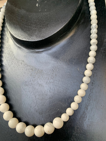 Howlite, 'collier/ chute de perle', de forme ronde de 4 à 10 millimètres de diamètre. 44 centimètres de longueur + 4 cm de rajout en chaînette. Fermoir de type 'mousqueton'. Très belle pièce !