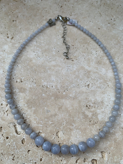 Agate Blue Lace, 'collier/ chute de perle', de forme ronde de 4 à 10 millimètres de diamètre. 44 centimètres de longueur + 4 cm de rajout en chaînette. Fermoir de type 'mousqueton'. Très belle pièce !