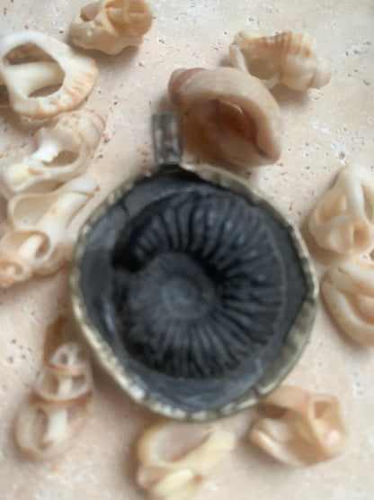 Ammonite fossile du Népal, taille de 45x35x12 millimètres. Pièce authentique et unique, révélant les spirales naturelles et les motifs fascinants de ce fossile. Livré avec cordon coulissant, prêt à porté ou à offrir !