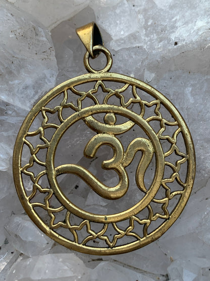 Om, pendentif en laiton doré de  3,6 centimètres de diamètre, vendu avec cordon noir réglable ! Tel un souffle ancien suspendu au creux du cœur, ce pendentif en laiton doré célèbre le symbole sacré Om, vibration originelle de l’univers !