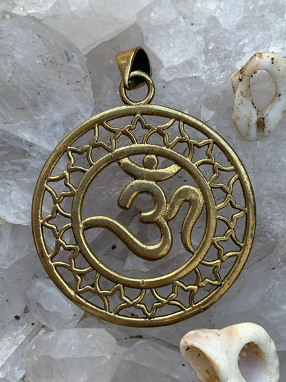 Om, pendentif en laiton doré de  3,6 centimètres de diamètre, vendu avec cordon noir réglable ! Tel un souffle ancien suspendu au creux du cœur, ce pendentif en laiton doré célèbre le symbole sacré Om, vibration originelle de l’univers !