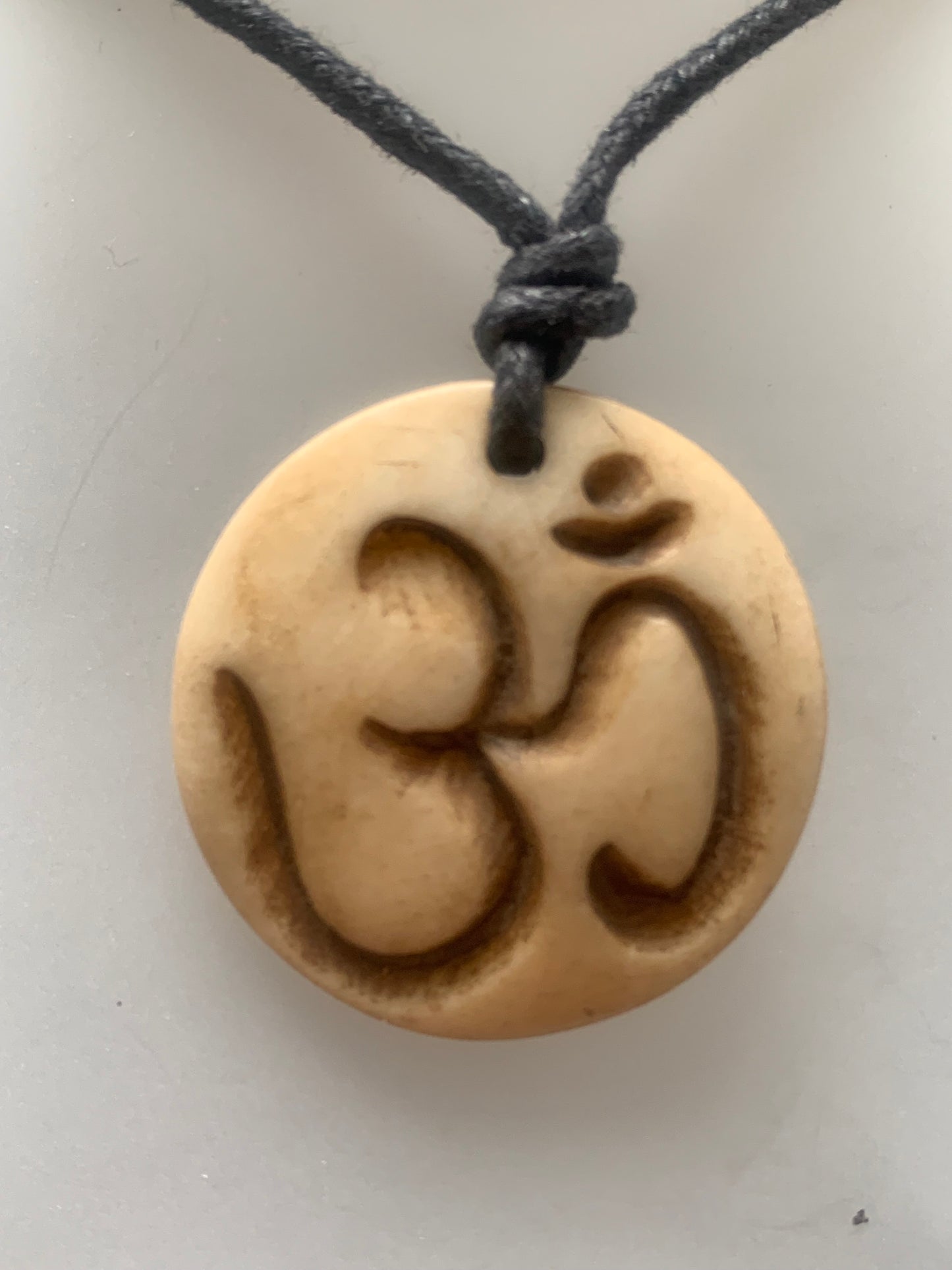 Pendentif artisanal du Népal avec symbole Om, sculpté dans de l’os, de 30 millimètres de diamètre x 4 mm d'épaisseur. Vendu avec cordon noir réglable offert, parfait !