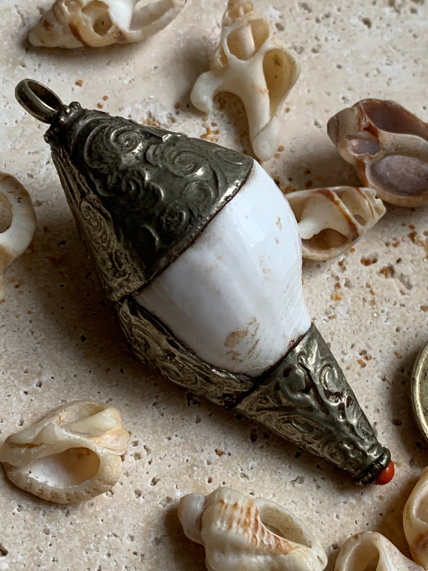 Pendentif artisanal du Népal en coquillage sertis en métal avec de jolies gravures et une perle de corail ! De 65 millimètres de hauteur x 28 mm de diamètre. Vendu avec cordon noir réglable offert, parfait !