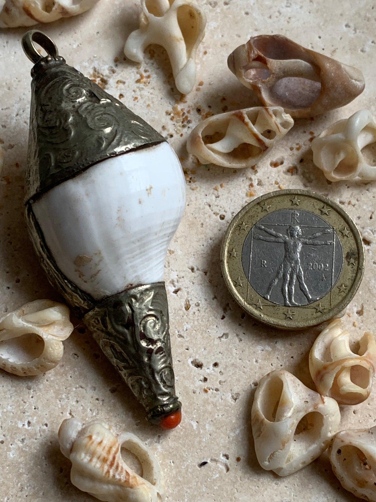 Pendentif artisanal du Népal en coquillage sertis en métal avec de jolies gravures et une perle de corail ! De 65 millimètres de hauteur x 28 mm de diamètre. Vendu avec cordon noir réglable offert, parfait !