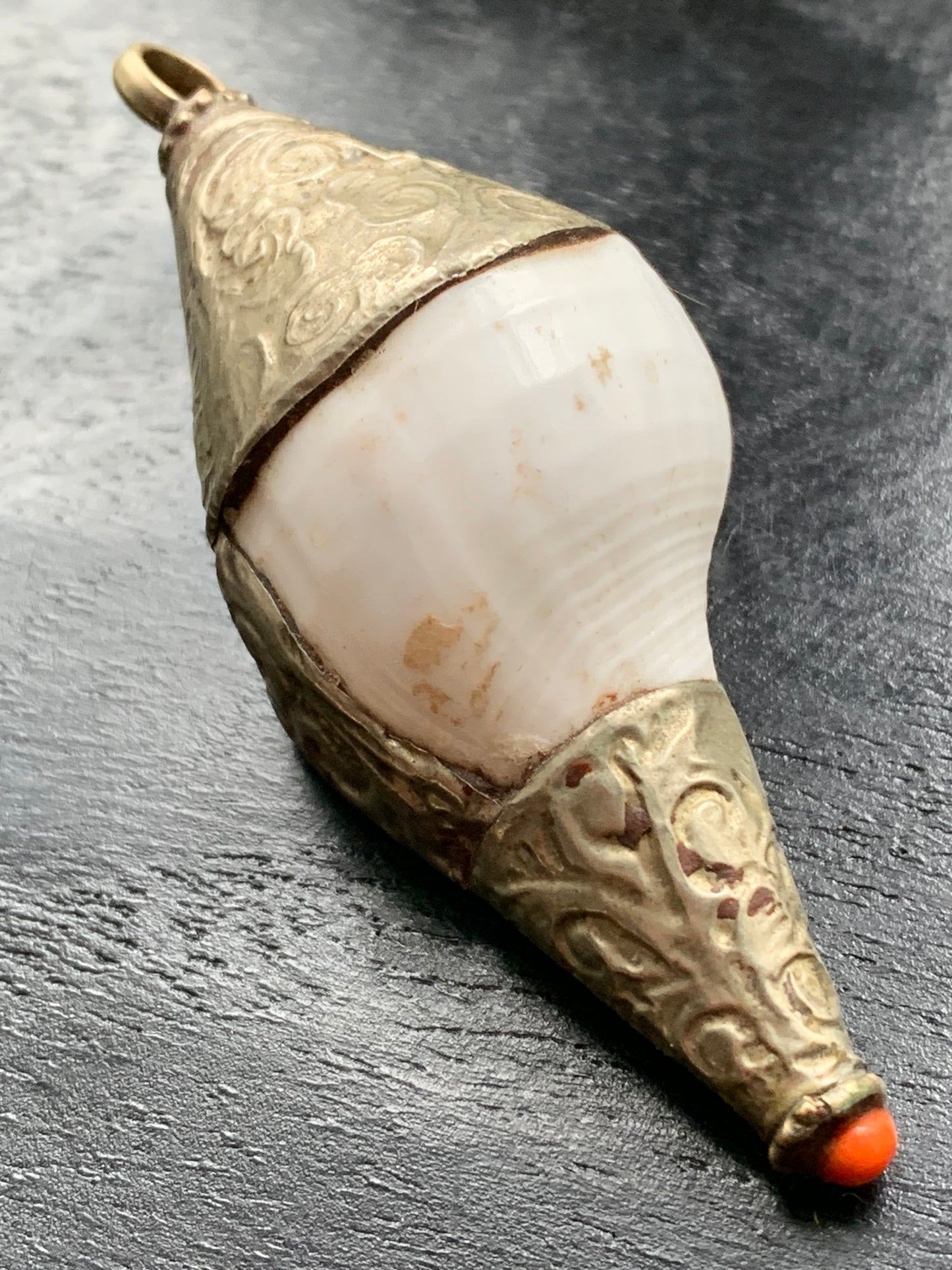 Pendentif artisanal du Népal en coquillage sertis en métal avec de jolies gravures et une perle de corail ! De 65 millimètres de hauteur x 28 mm de diamètre. Vendu avec cordon noir réglable offert, parfait !