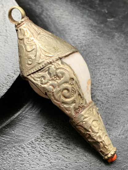 Pendentif artisanal du Népal en coquillage sertis en métal avec de jolies gravures et une perle de corail ! De 65 millimètres de hauteur x 28 mm de diamètre. Vendu avec cordon noir réglable offert, parfait !