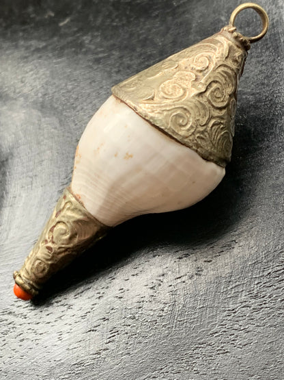 Pendentif artisanal du Népal en coquillage sertis en métal avec de jolies gravures et une perle de corail ! De 65 millimètres de hauteur x 28 mm de diamètre. Vendu avec cordon noir réglable offert, parfait !