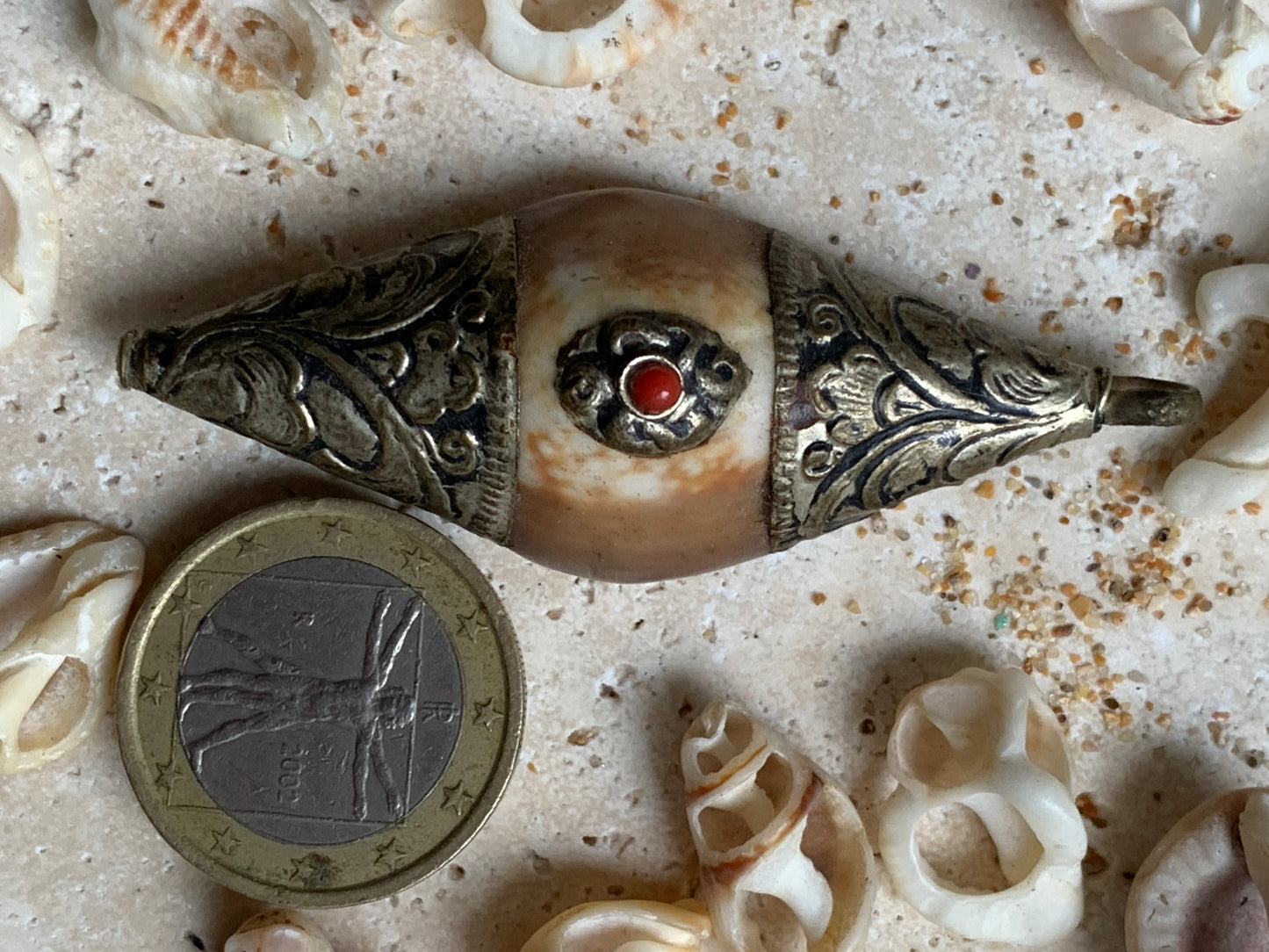 Pendentif artisanal du Népal en coquillage sertis en métal avec de jolies gravures et une perle de corail ! De 60 millimètres de hauteur x 23 mm de largeur x 16 d'épaisseur. Vendu avec cordon noir réglable offert, parfait !