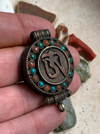 Pendentif/ Reliquaire artisanal du Népal avec pierres de turquoise et de corail sertis sur métal avec jolie gravure du Om ! De 52 millimètres de hauteur x 35 mm de largeur x 11 d'épaisseur. Vendu avec cordon noir réglable offert, parfait !