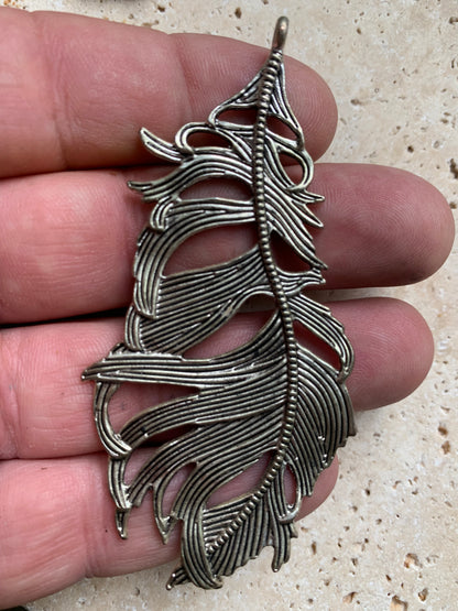 Pendentif en métal argenté en forme de plume. De 85 x 40 x 5 millimètres. Vendu avec cordon noir réglable offert, parfait !
