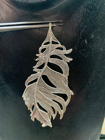Pendentif en métal argenté en forme de plume. De 85 x 40 x 5 millimètres. Vendu avec cordon noir réglable offert, parfait !