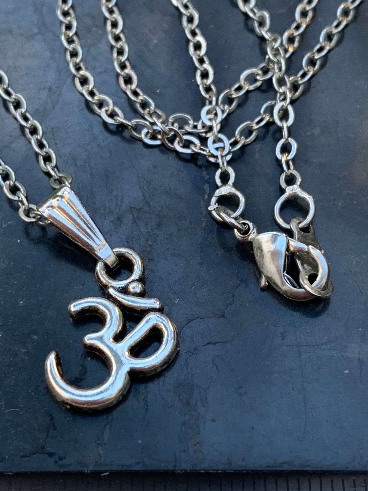 Om, pendentif en laiton argenté, de 23x12x2 millimètres -1,3 gr. Vendu avec cordon noir réglable offert, parfait !